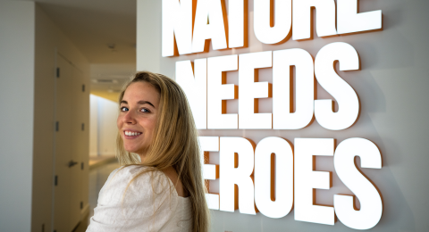 Katie Rascoe ‘22 poses in front of neon sign that reads "Nature needs heroes" in Timberland's lobby.