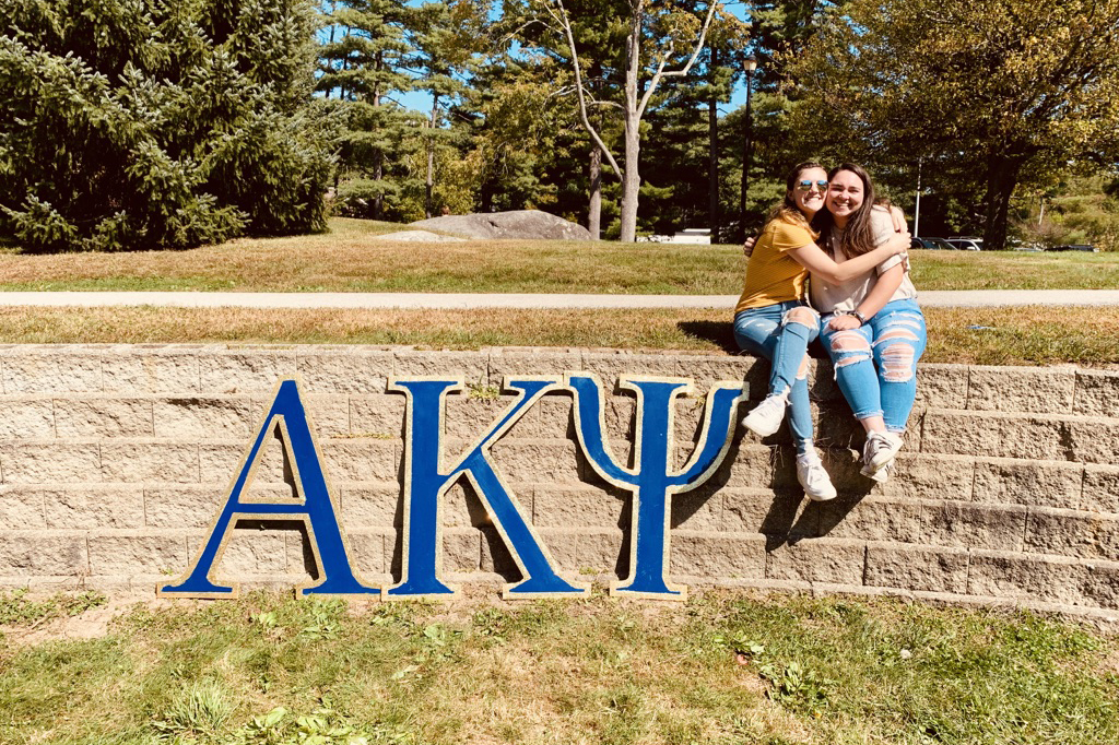 Two female students pose next to an AKPsi sign