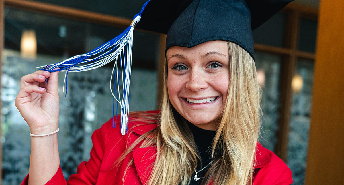 Emma Battisellio smiles at the camera while holding out the tassel of a graduation cap