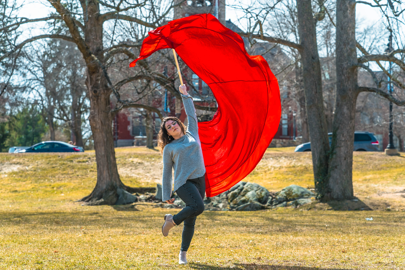 A student swinging a large red color guard flag