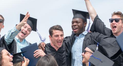 Students at commencement ceremony celebrating with hands in the air 