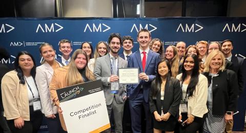 A large group of UNH Marketing majors gathers for a photo opportunity at the American Marketing Association's International Collegiate Competition. One student holds a sign that reads, "Competition finalist."