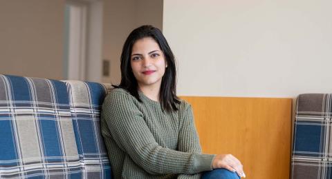 Analytical economics major Dija Haq sits on a couch in the UNH MUB, legs crossed, with a small smile for the camera.