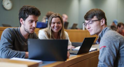 Three UNH Analytical Economics students and members of Artifex Data Analytics Club gather around a laptop in a Paul College classroom.