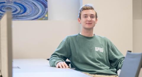 Marketing and Finance major Ian Lidster sits at a table in the UNH ECenter, smiling at the camera.