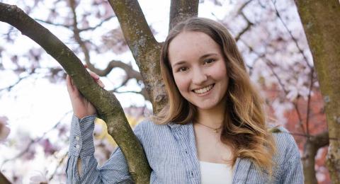 Analytical Economics major Skye Loto stands with her arm wrapped around a blossoming tree, smiling at the camera.