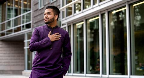 UNH International Business and Economics major Fazla Karim stands outside in the Paul College courtyard, hand over his heart, smiling off camera.
