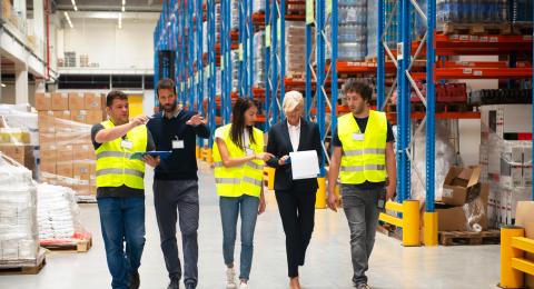 five people are walking though a warehouse checking product for manage the supply chain