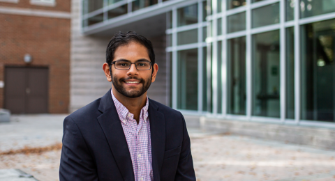 A male student smiles at the camera while seated in Paul College's outdoor courtyard.