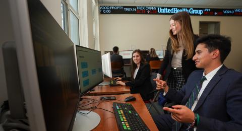 Three students chat in Paul College's bloomberg terminal room.