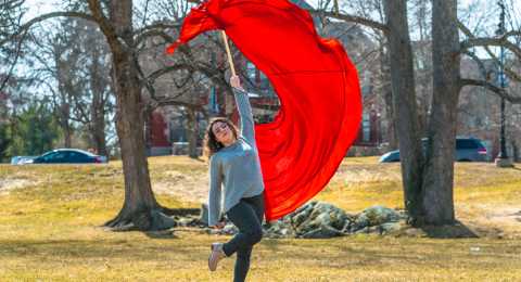 A student swinging a large red color guard flag