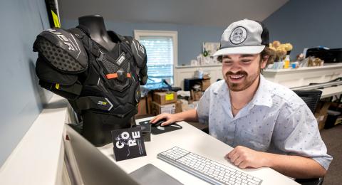 Ryan Meader '22 works at his laptop next to a mannequin wearing Helios Hockey technology.