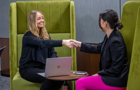 A student shakes the hand of a professional while seated in green armchairs.