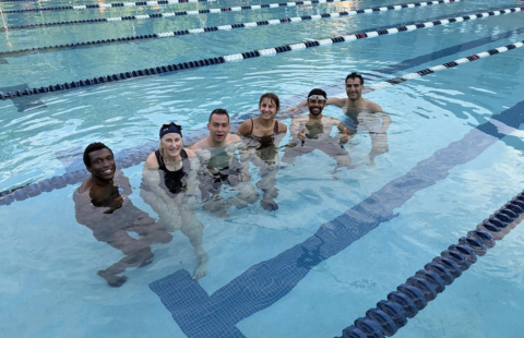 Paul College graduate students and colleagues pose together at the UNH Outdoor Pool after participating in an adult swim class.