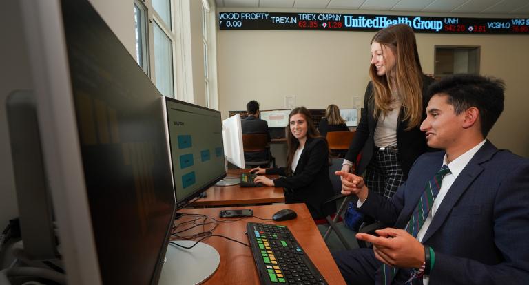 Three students chat in Paul College's bloomberg terminal room.