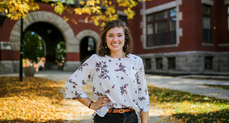 A female student smiles at the camera with her right arm on her left hip