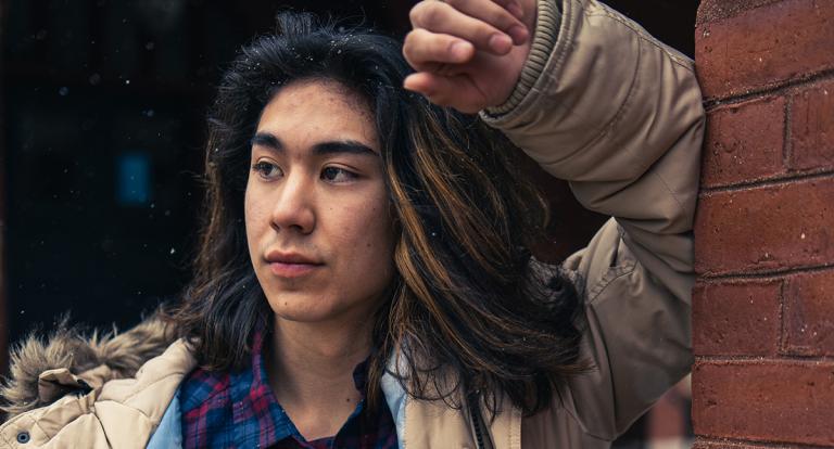 Kiyoshi Dustin leans against a wall outside Thompson Hall on campus.