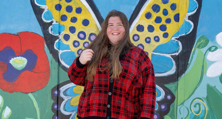 Emily Alberigo stands in front of a butterfly wing mural and smiles