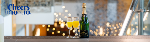 A bottle of Peter T. Paul Champagne next to two champagne flues filled with mimosas at the top of the staircase leading to the Great Hall. In the background, twinkle lights.
