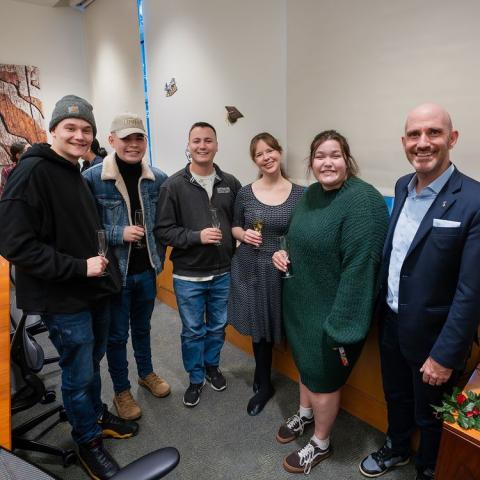 Fours student pose for a photograph with faculty; they are holding champagne glasses in their hands and all are smiling.