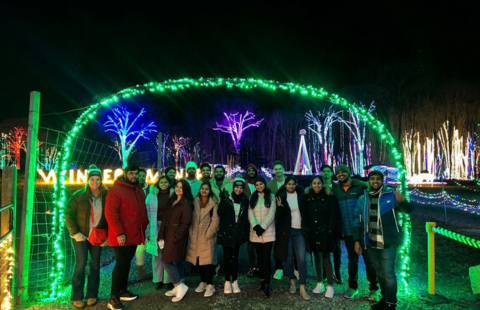 A group of international students and staff from the Paul Graduate Programs office pose in their winter jackets under an arched display of green christmas lights