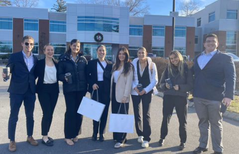 Eight students who are dresses professionally pose outside of the Medicus building