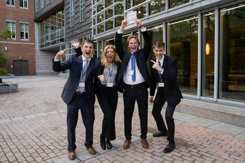 Four students hold a plaque into the air and cheer