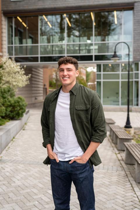 Accounting major Patrick Yudkin stands outside UNH Paul College in the courtyard, hands in his pockets, smiling at the camera.