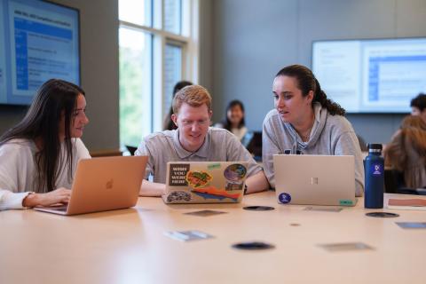 Three marketing majors gather around their laptops in a UNH Paul College classroom as part of the American Marketing Association Collegiate Chapter.