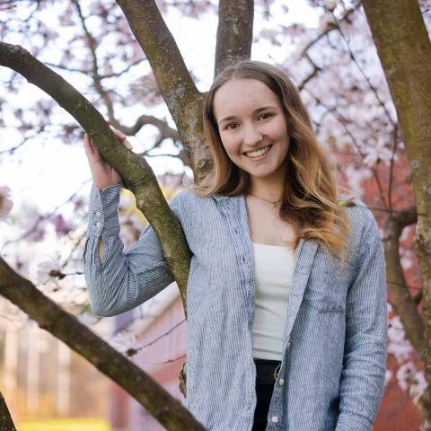 Analytical Economics major Skye Loto stands with her arm wrapped around a blossoming tree, smiling at the camera.