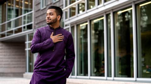 UNH International Business and Economics major Fazla Karim stands outside in the Paul College courtyard, hand over his heart, smiling off camera.