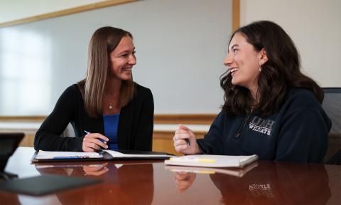 A female student and staff member chat and smile in a UNH Paul College conference room.