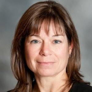 Professional headshot of Beth Scarborough with medium-length hair, wearing a dark top, facing forward against a neutral gray background.