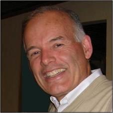 Professional headshot of Wayne Morrison smiling, wearing a light sweater over a collared shirt, with an indoor background.
