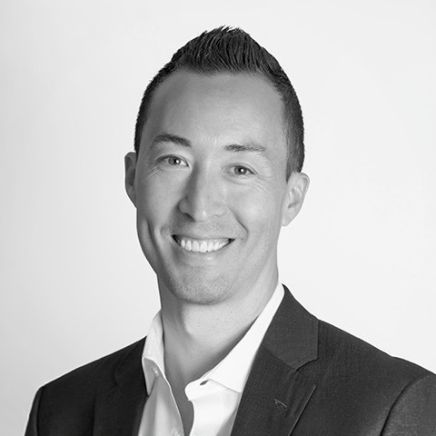 Black-and-white professional headshot of Todd Boucher in a suit jacket and collared shirt, facing forward against a plain light background, with a slight smile.