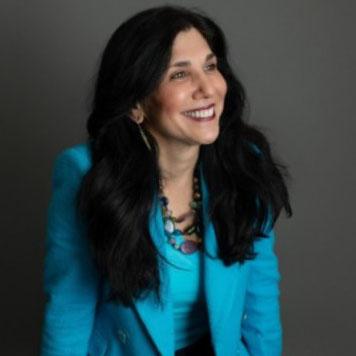 Headshot of Linda Faranas with long dark hair, wearing a teal blazer and necklace, seated against a neutral background.