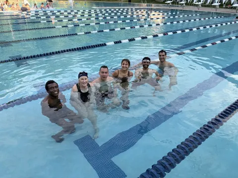 Paul College graduate students and colleagues pose together at the UNH Outdoor Pool after participating in an adult swim class.