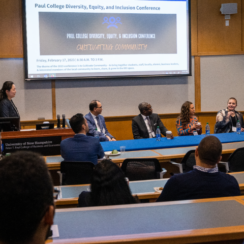 Panelists sit in front of a projector screen titled "Paul College Diversity, Equity and Inclusion Conference" with a moderator to the left, and students facing them, seated at desks.