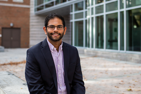 A male student smiles at the camera while seated in Paul College's outdoor courtyard.