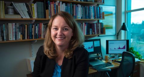 Close up of Reagan Baughman in her office, bookshelf and computer behind her