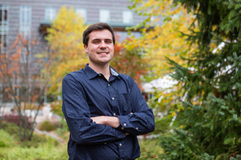 Bob Horgan '22 Male student crossing his arms and smiling at the camera in front of the Paul College courtyard