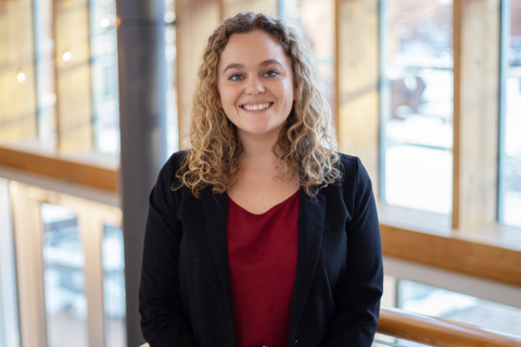 A female student dressed in business attire smiles at the camera.