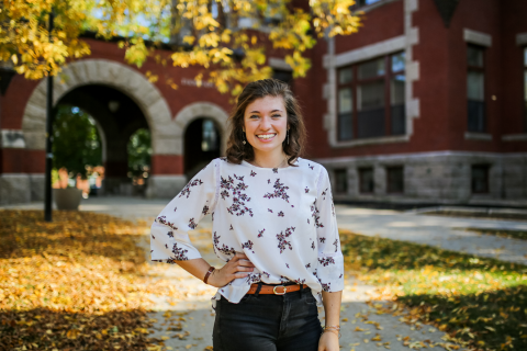 A female student smiles at the camera with her right arm on her left hip