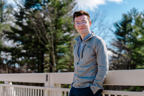 A male student leans against a railing with his hands in his pockets.