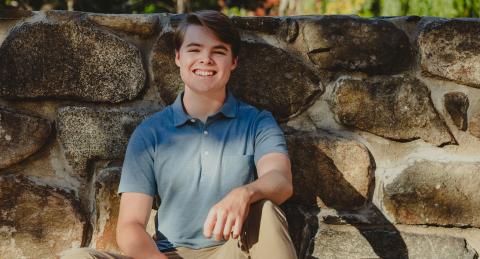 Gavin Blonda smiles as he leans against a stone wall