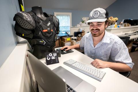 Ryan Meader '22 works at his laptop next to a mannequin wearing Helios Hockey technology.